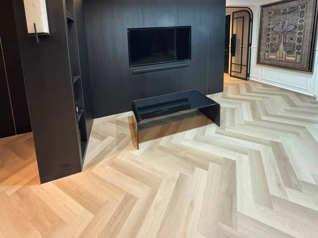 Carrera Oak herringbone vinyl flooring in a living room with a dark TV feature wall